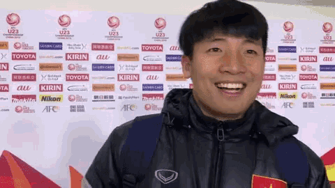 a man is smiling in front of a wall with logos for toyota kirin and nikon