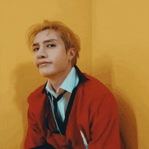 a man wearing a red sweater and tie is leaning against a wall