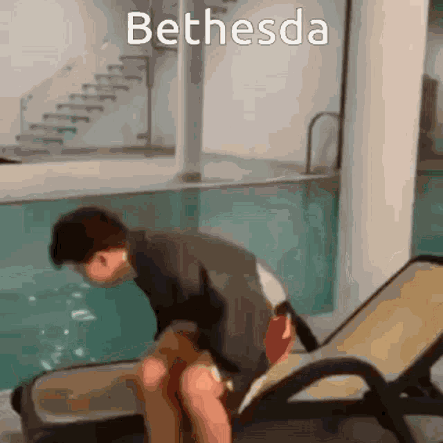 a man is sitting on a chair in front of a swimming pool with the word bethesda above him