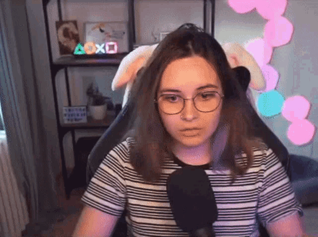 a girl wearing glasses and a striped shirt is sitting in front of a microphone in a room .