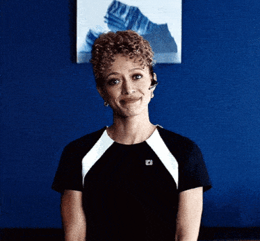 a woman with curly hair is smiling in front of a blue wall with a picture on it