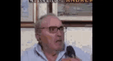 a man wearing glasses is speaking into a microphone in front of a sign that says " andrea "
