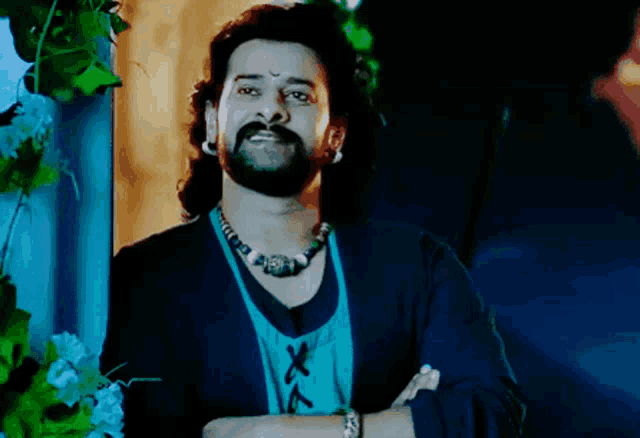 a man with a beard is wearing a necklace and a blue shirt