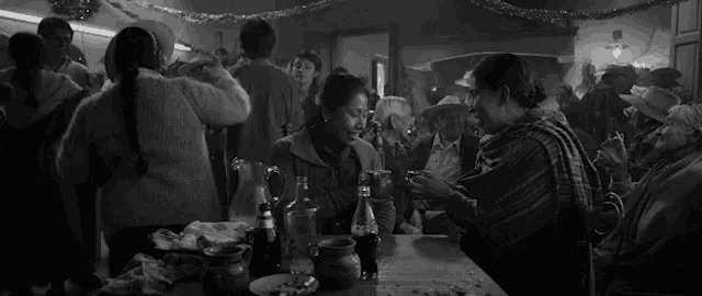 a black and white photo of a group of people sitting around a table .
