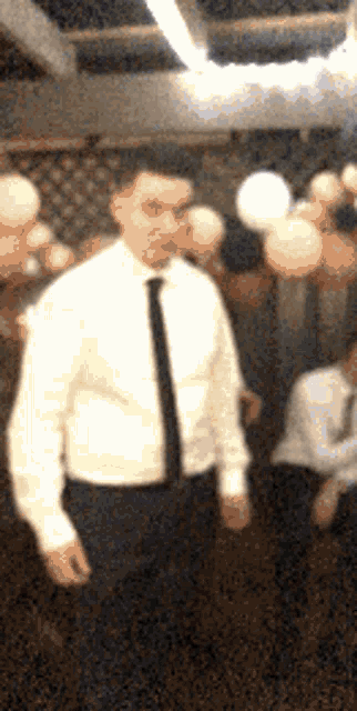 a man in a white shirt and black tie is standing in a room with balloons hanging from the ceiling