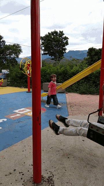 a little girl in a pink shirt stands next to a red pole with the letter d painted on it