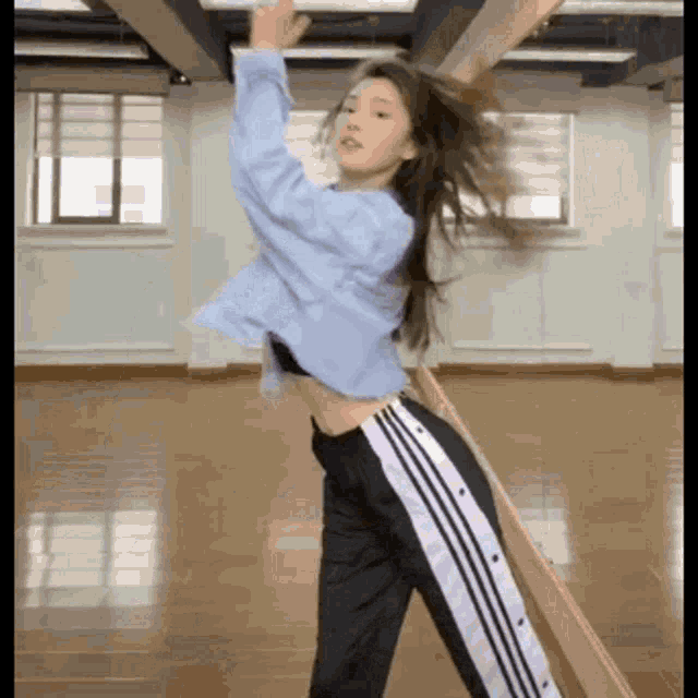 a girl in a blue shirt and black pants is dancing in a room