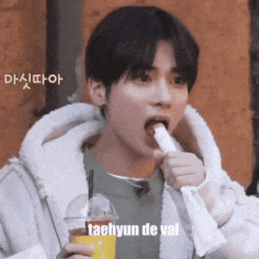 a young man is holding a cup of coffee and eating a piece of food with a caption that says taehyun de val