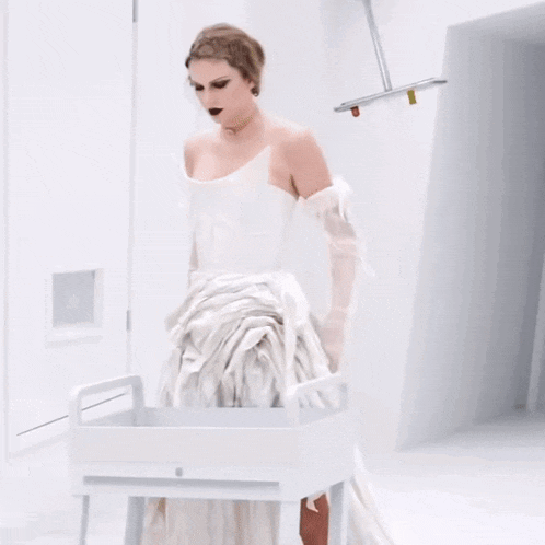 a woman in a white dress and gloves is standing in a white room .