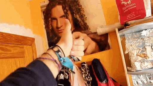 a person is giving a thumbs up in front of a poster of a man with curly hair