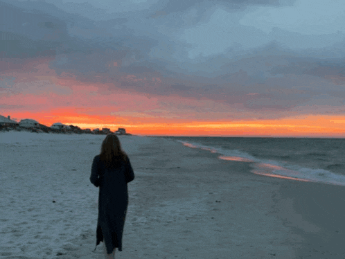 a woman standing on a beach looking at the sunset