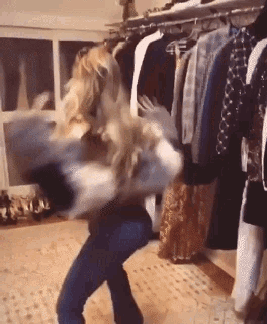 a woman is dancing in a closet with clothes hanging on a rack .
