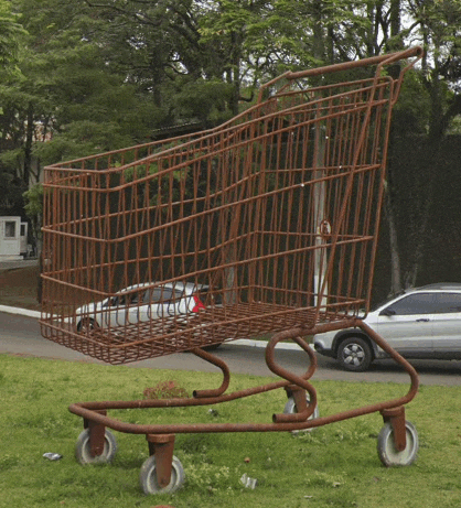 a large shopping cart is sitting in the grass in front of a car