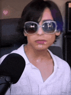 a woman wearing sunglasses and a white shirt is sitting in front of a microphone .