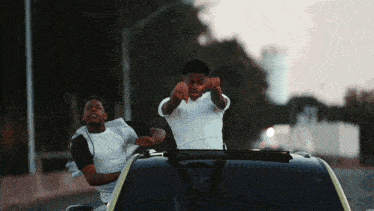 two men are standing in front of a car and one is pointing