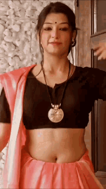 a woman wearing a pink saree and a black crop top is standing in front of a door .