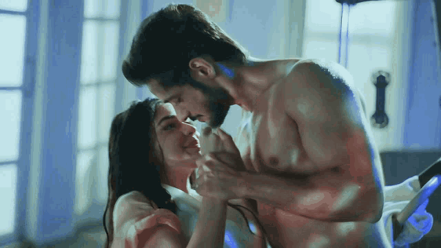 a shirtless man and woman are kissing in a room