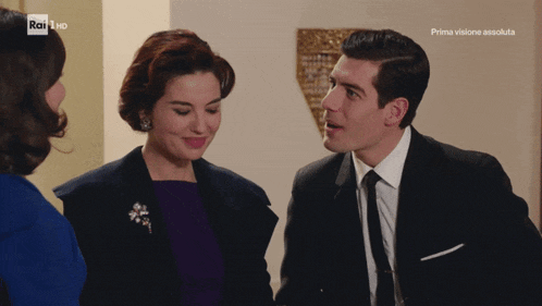 a man in a suit and tie stands next to a woman in a blue dress and a woman in a purple dress