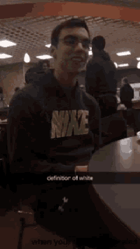 a man wearing a nike shirt sits at a table looking at his phone