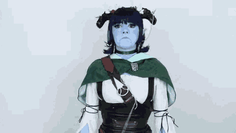 a woman in a costume with blue face paint and horns is standing in front of a white background .