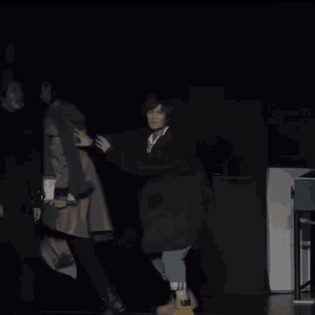 a group of people are standing on a stage in a dark room holding hands .