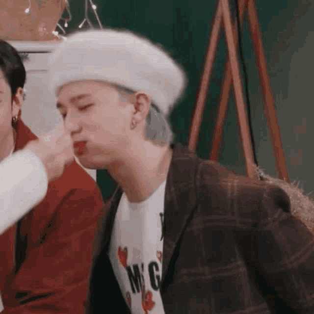 a man wearing a white beret and a plaid jacket is being kissed by a woman .
