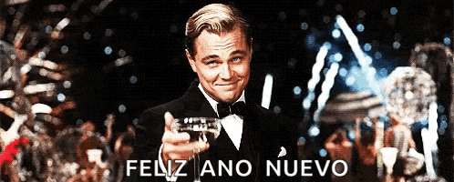a man in a tuxedo is holding a glass of champagne in front of a sign that says " feliz ano nuevo "
