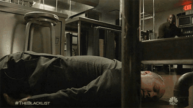 a man is laying on the floor in a kitchen with a nbc logo in the background