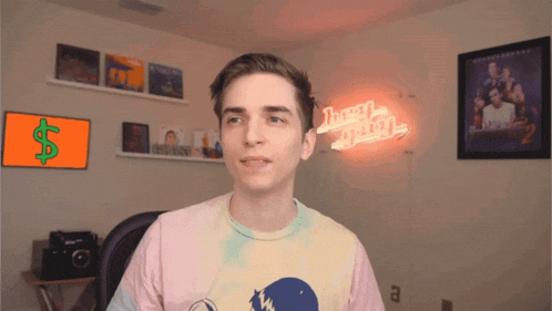 a man wearing a tie dye shirt is standing in front of a neon sign that says juan pablo