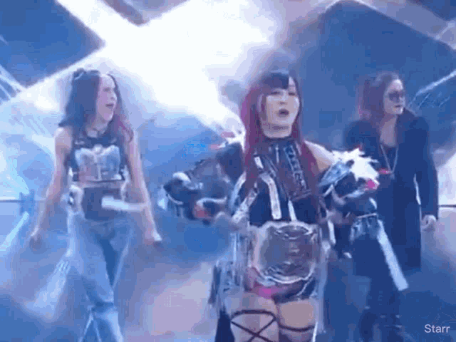 a group of female wrestlers are standing on a stage holding a championship belt .
