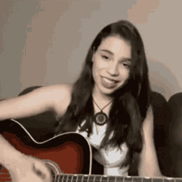 a woman is sitting on a couch playing an acoustic guitar and smiling .