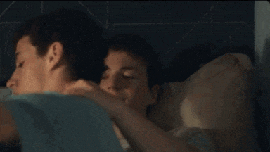 a couple of young men are laying in bed hugging each other .