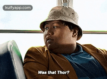 a man wearing a hat is sitting on a bus and says `` was that thor ? ''