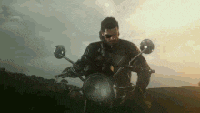 a man in a leather jacket is riding a motorcycle on a country road .