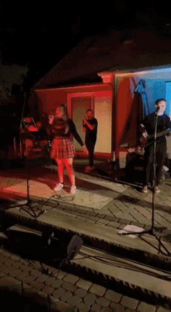 a woman in a plaid skirt sings into a microphone while a man plays a guitar