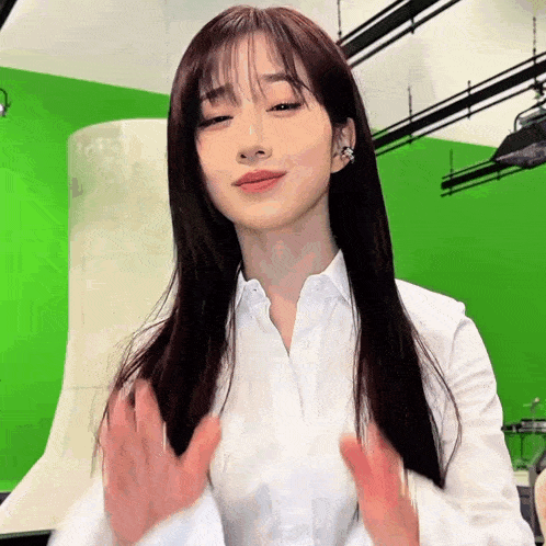 a woman in a white shirt is standing in front of a green screen and making a funny face .