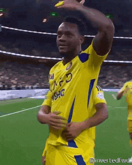 a soccer player wearing a yellow jersey with a blue stripe on the sleeves