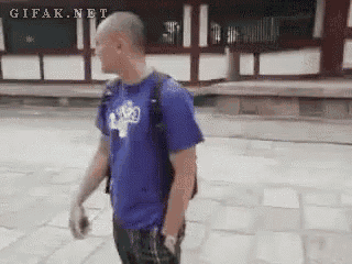 a man in a blue shirt is walking down a sidewalk with a backpack .