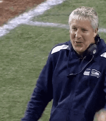 a man wearing a seattle seahawks jacket is standing on a football field .