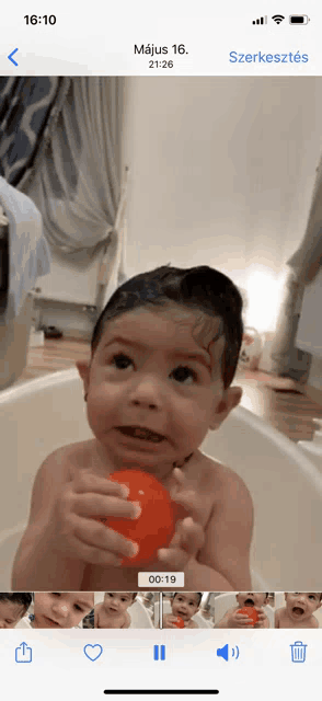a phone screen shows a baby in a bathtub holding a ball
