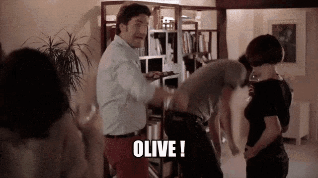 a group of people are dancing in a room and one of them is saying " olive "