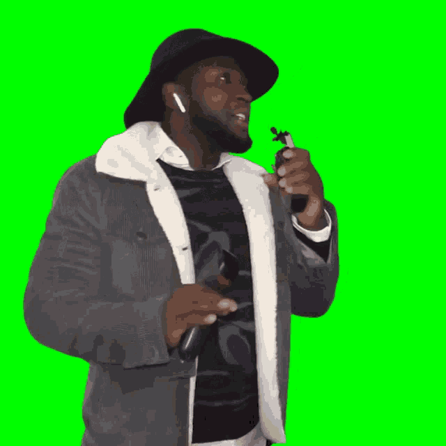 a man wearing a hat and ear buds stands in front of a green background