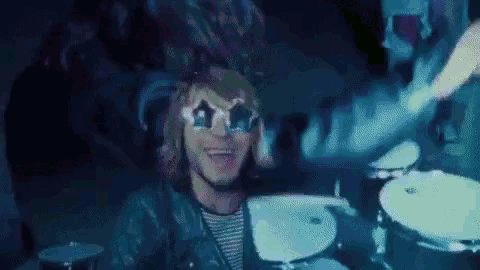 a man wearing sunglasses is playing drums in a dark room with a ghost behind him .