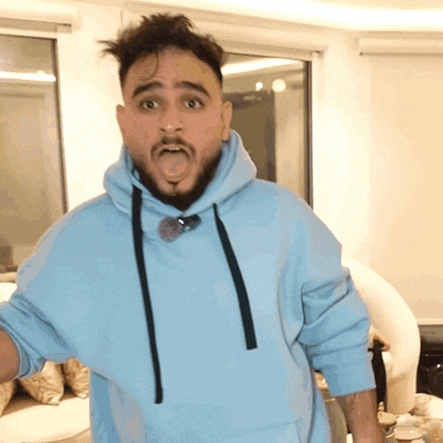 a man with a beard is wearing a light blue hoodie and making a funny face