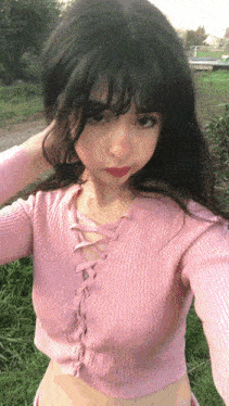 a girl in a pink sweater is taking a selfie in a field