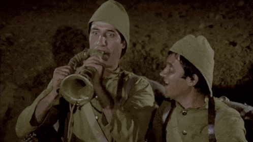 a man blowing a trumpet next to another man wearing a hat