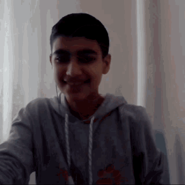a young boy wearing a grey hoodie with a paw print on it smiles for the camera