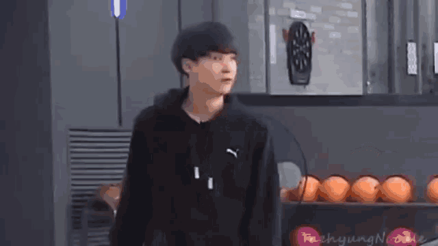 a young man in a black puma hoodie is standing in front of a dart board