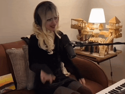 a woman singing into a microphone while sitting on a couch next to a keyboard