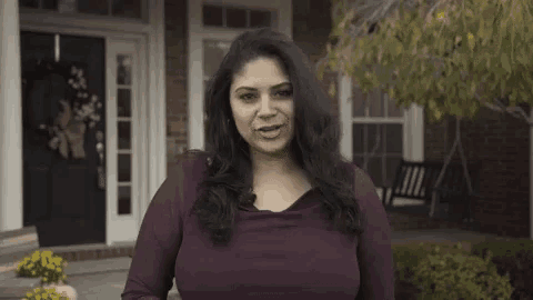 a woman is standing in front of a brick house and making a funny face .